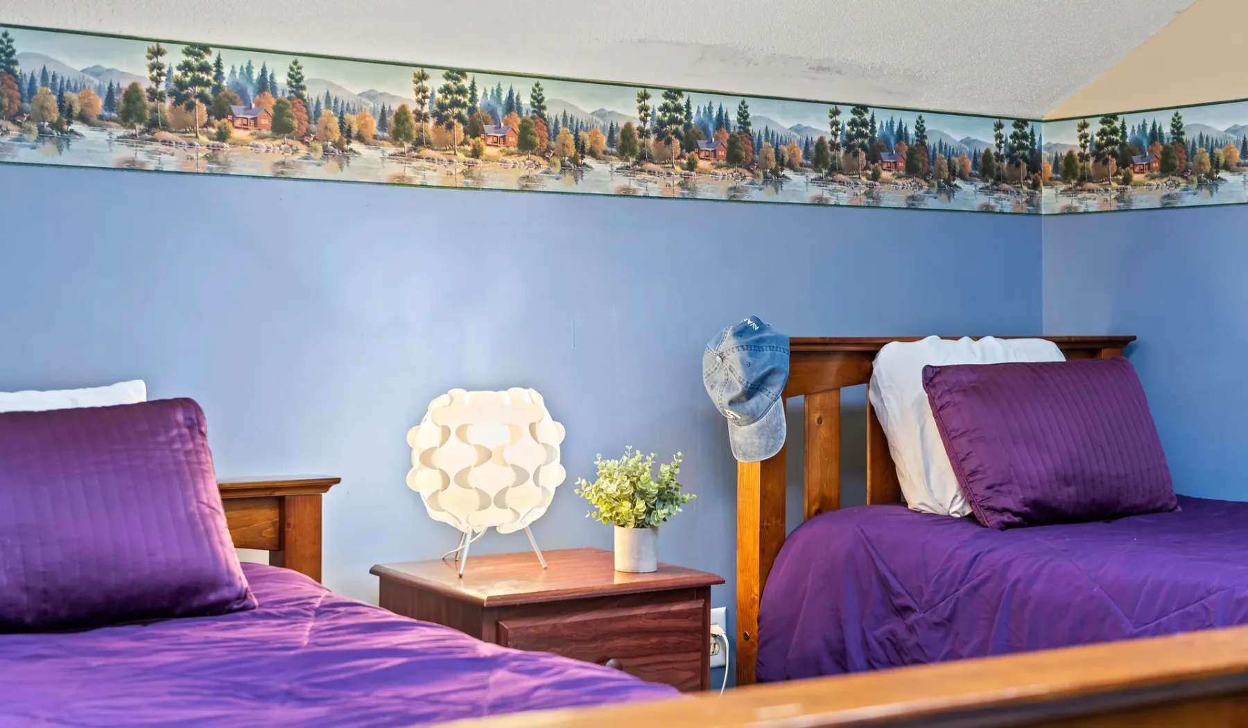 Un dormitorio con dos camas, ropa de cama morada y una mesita entre ellas.
