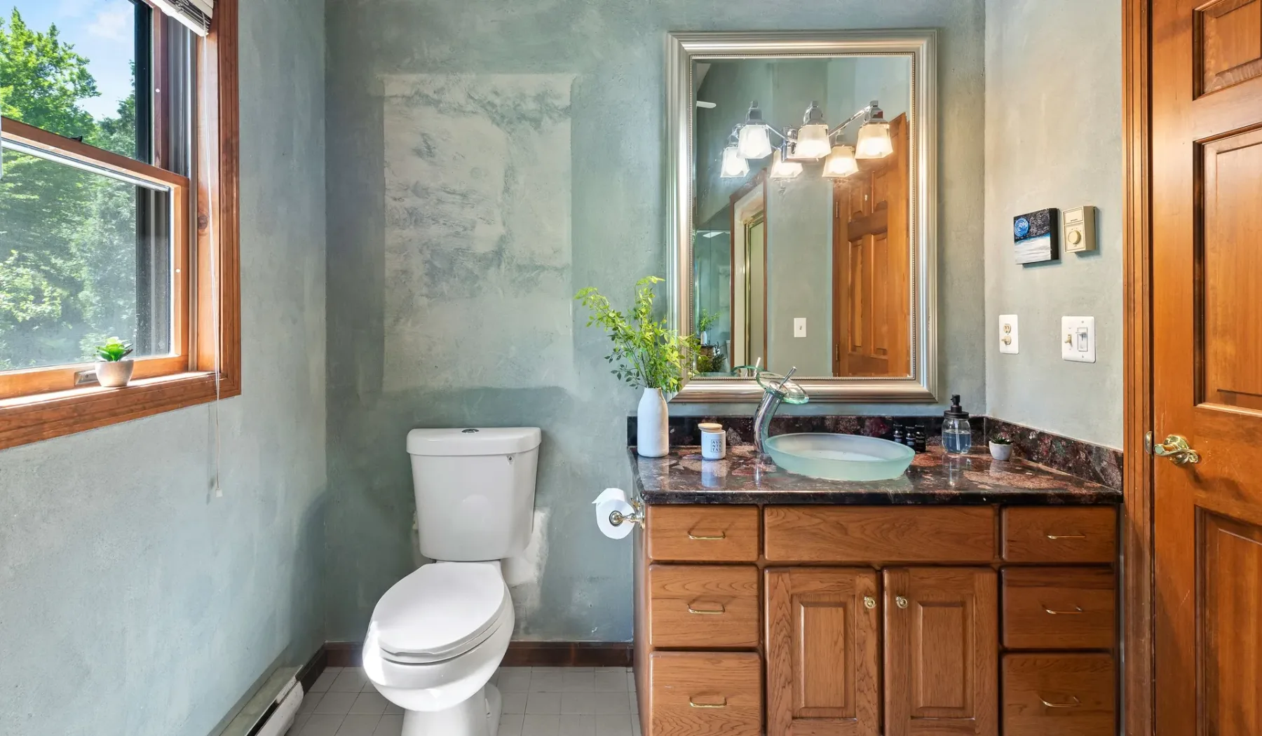 Un baño con inodoro, lavabo y tocador de madera junto a una ventana.