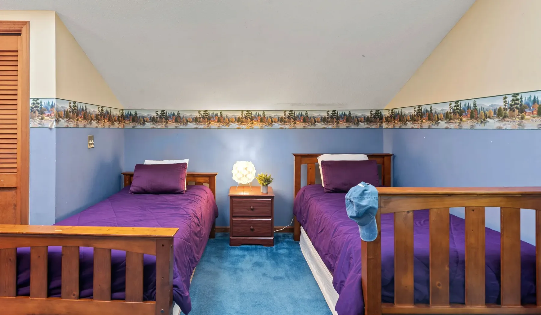 Un dormitorio con dos camas, ropa de cama morada y una mesita de madera.