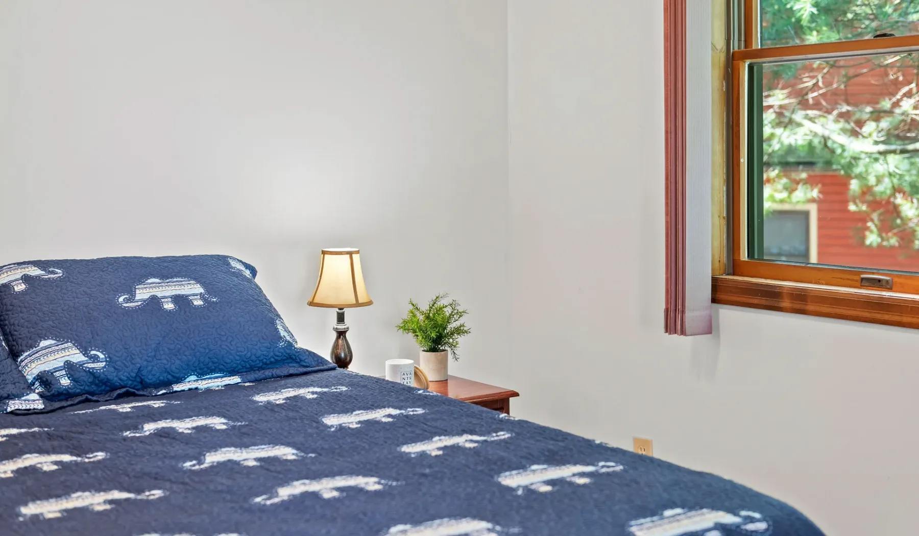 Un dormitorio con una cama cubierta con una manta azul estampada junto a una ventana.