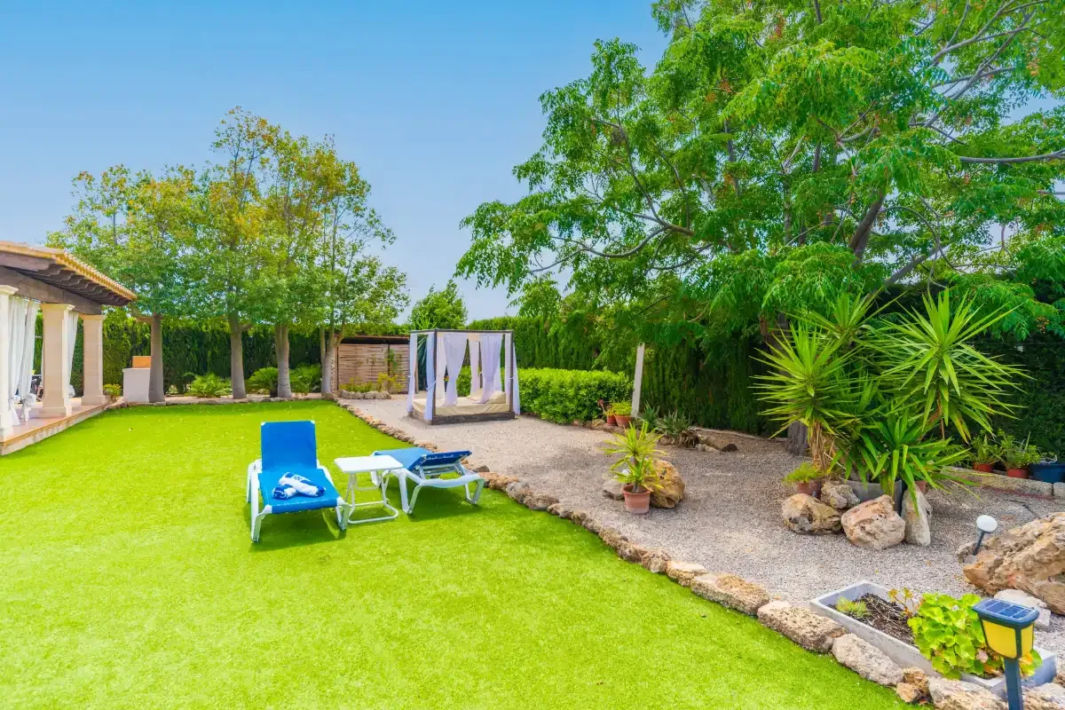 A sunny garden with green lawn, lounge seating, and leafy trees.