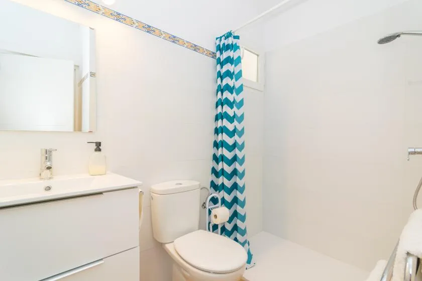 A bathroom with a sink, toilet, and teal patterned shower curtain.