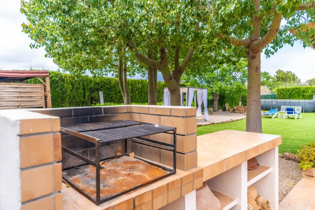 A brick outdoor barbecue sits beside a tree-shaded lawn.