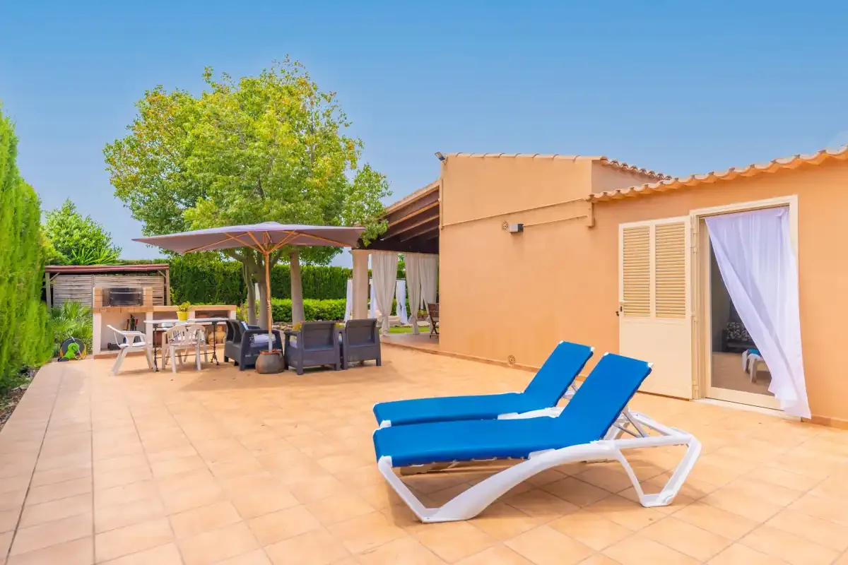 A sunny patio has blue lounge chairs, shaded seating, and a curtained doorway.