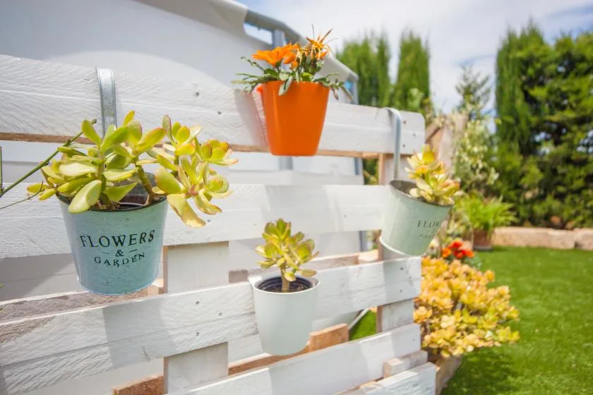 A white garden fence holds colorful potted flowers beside a green lawn.
