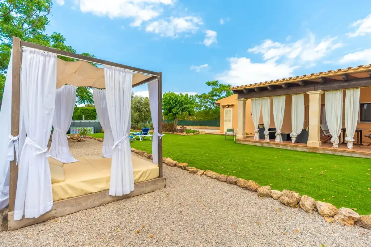 An outdoor garden lounge with a curtained daybed beside a lawn.