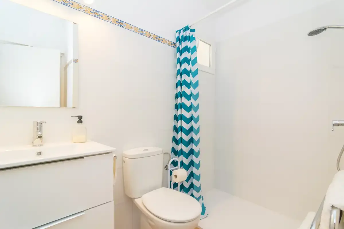 A bathroom with a sink, toilet, and shower behind a patterned curtain.