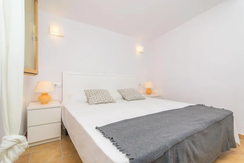 A bright bedroom with a neatly made bed and gray blanket.