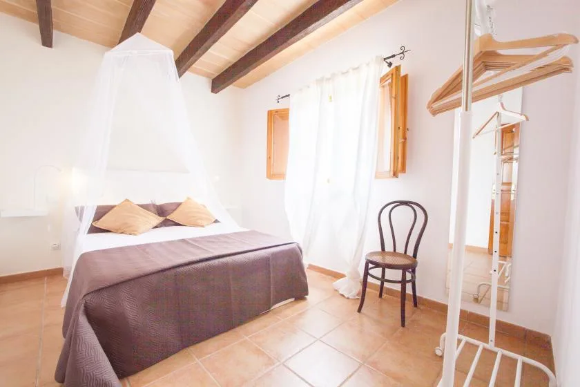 A bright bedroom with a curtained bed, a chair, and a clothes rack.