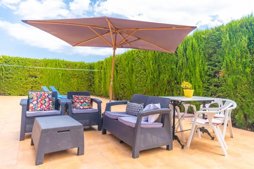 An outdoor patio has seating and a dining table beneath a large umbrella.
