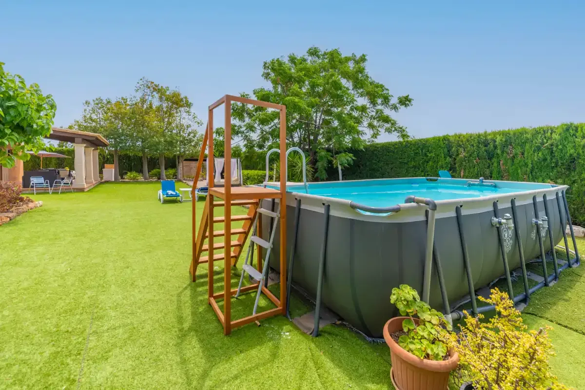 An outdoor swimming pool sits on a lawn beside a wooden ladder.