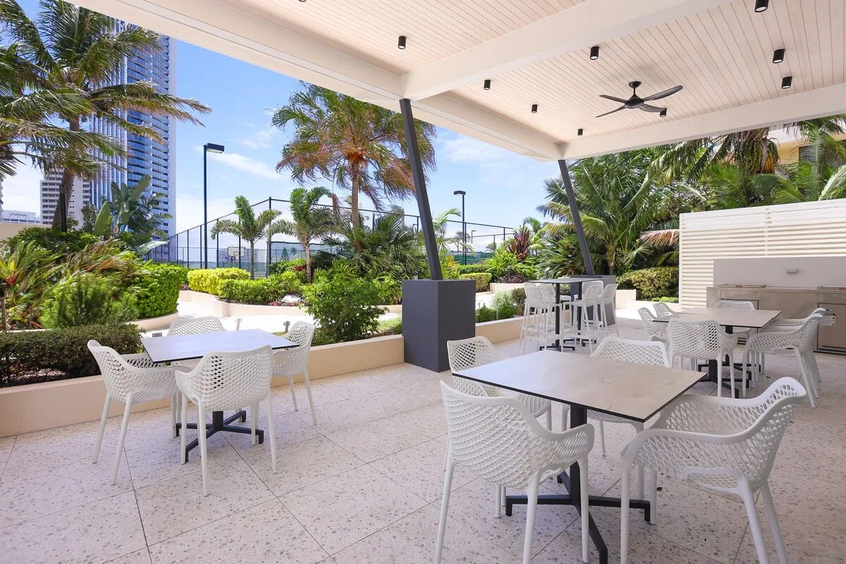 A covered outdoor dining area with white tables and seating among tropical plants.