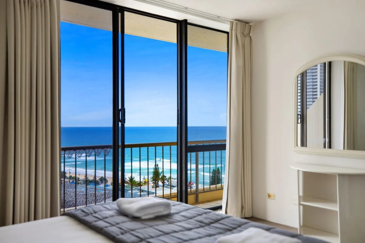 Dormitorio con una cama junto a grandes ventanas con vistas al mar.