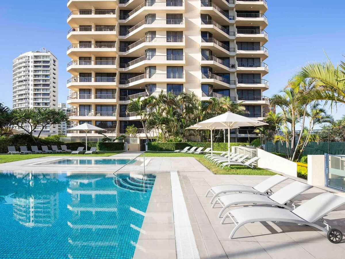 Outdoor swimming pool with lounge seating beside a high-rise building.