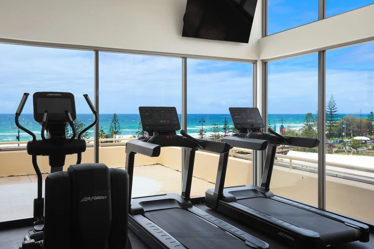 A gym with treadmills and an exercise bike faces the ocean through large windows.