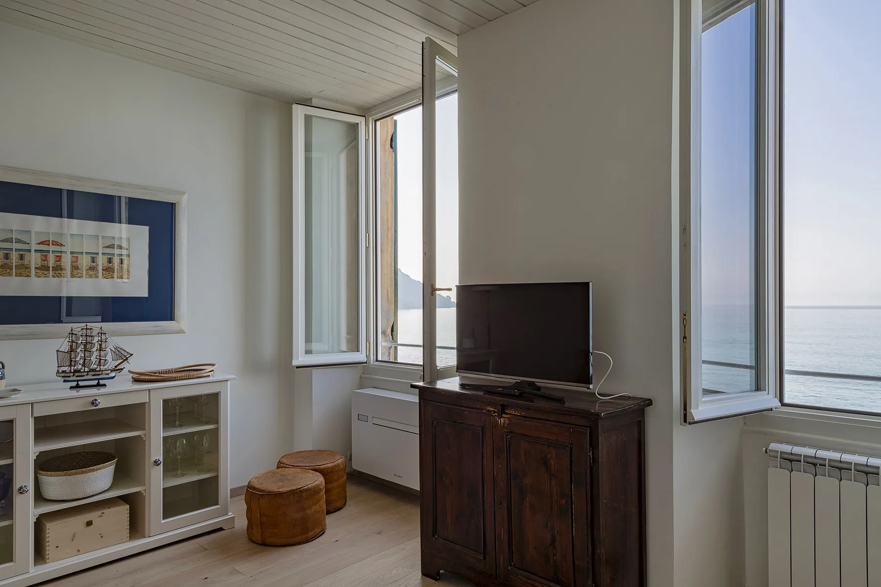 Una sala luminosa con un mueble para televisión y ventanas abiertas con vistas al agua.