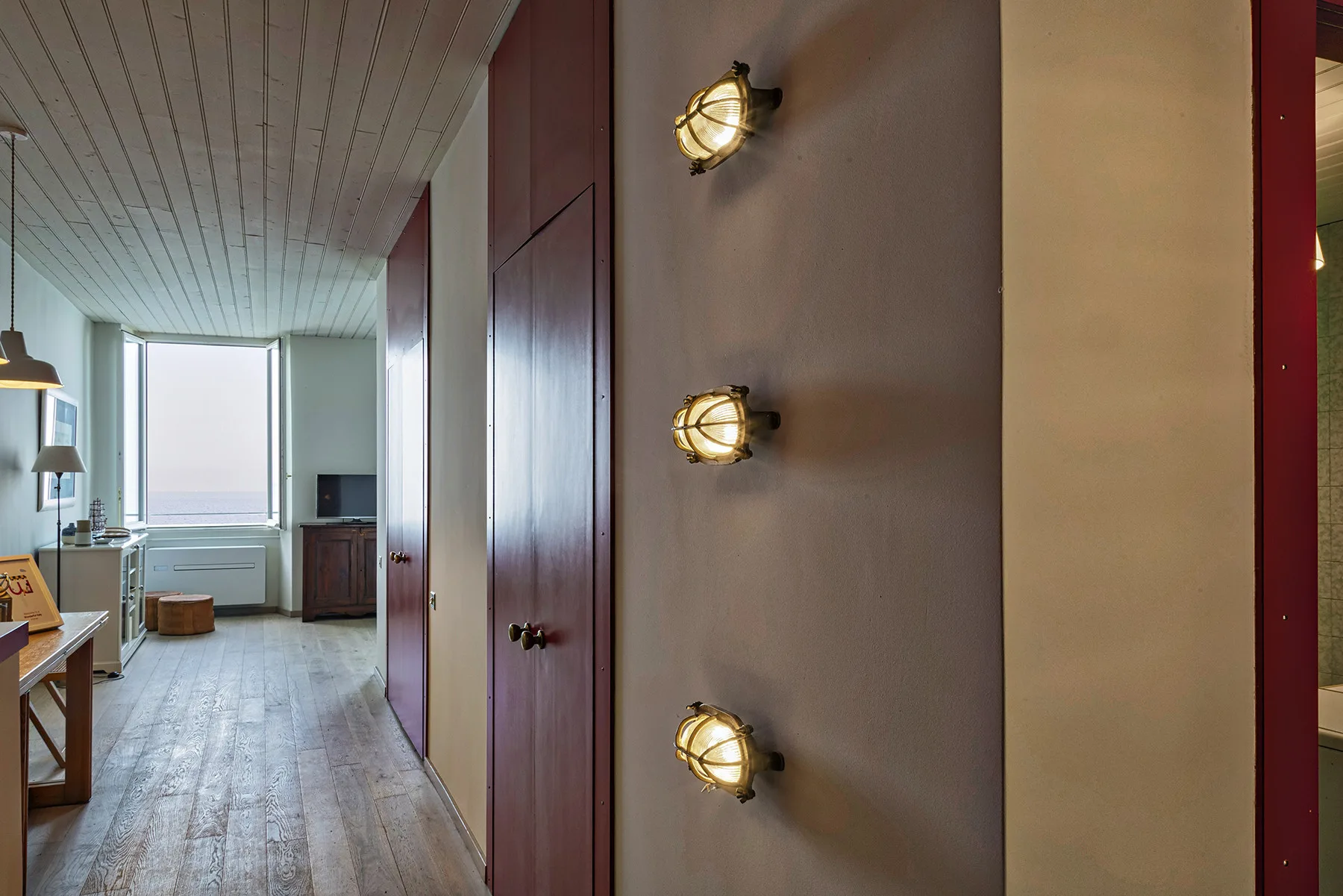 Un pasillo interior estrecho conduce a una habitación luminosa con una ventana grande.