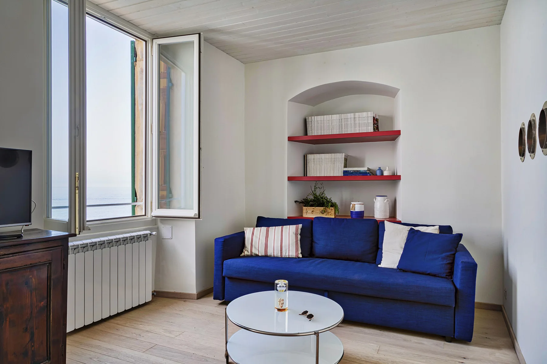Una sala de estar con asientos azules, una mesa de centro redonda y una ventana abierta.