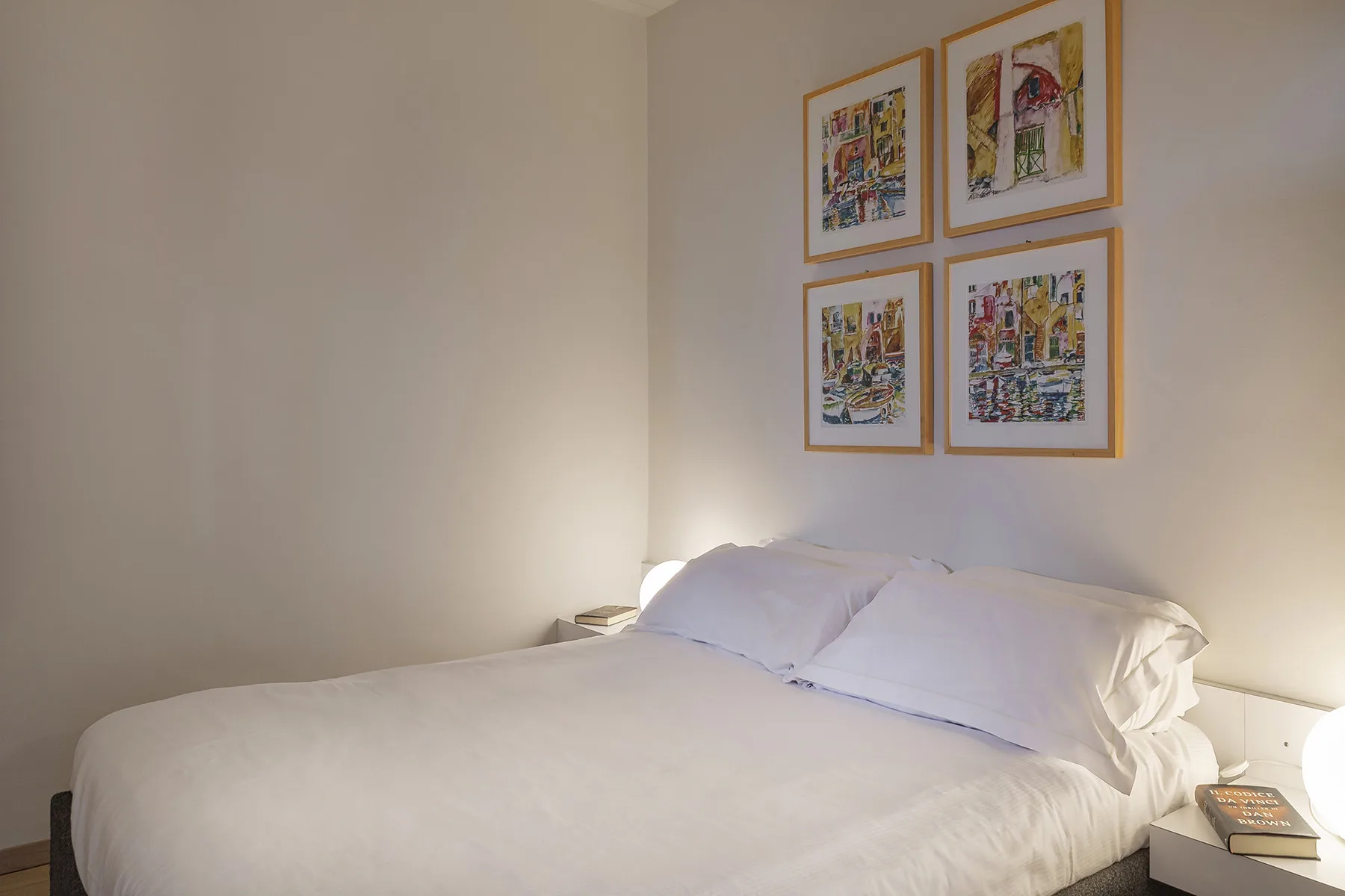 Un dormitorio con una cama bien arreglada y cuadros enmarcados encima.