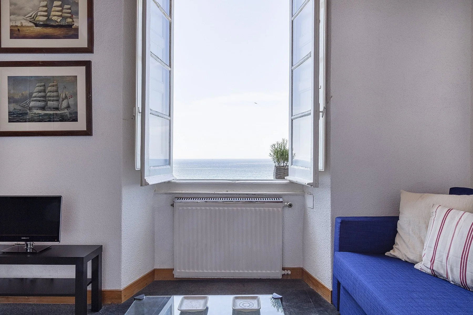 Una sala de estar con asientos azules junto a una ventana abierta con vistas al mar.