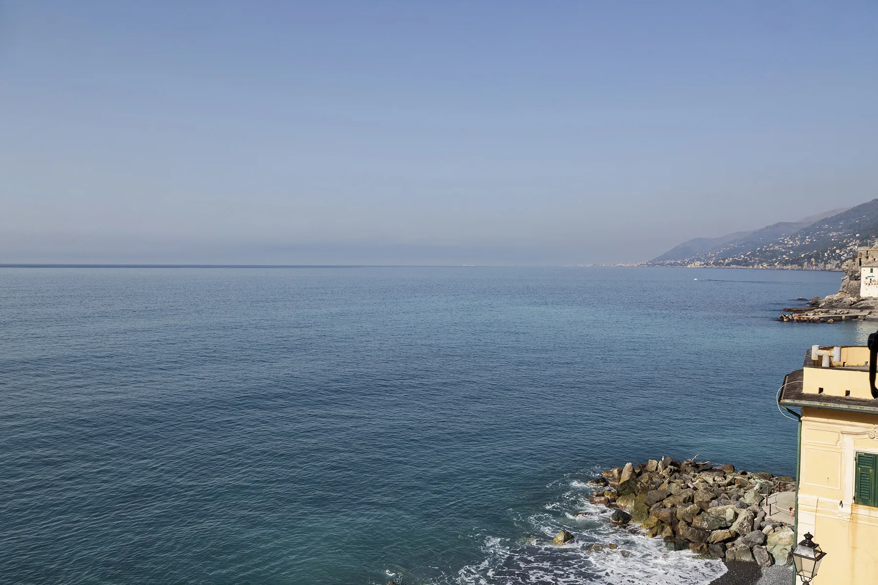 Un paisaje marino se extiende hacia una costa distante, con rocas junto al agua.