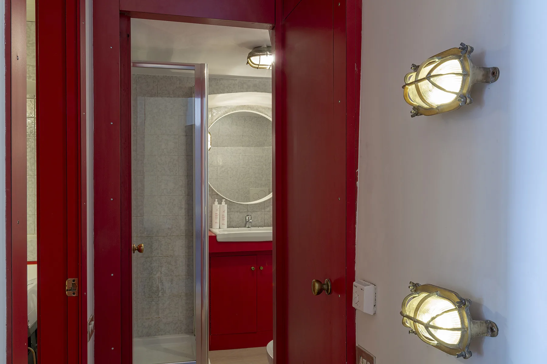 Se ve un baño a través de una puerta roja abierta, con lavabo y ducha.