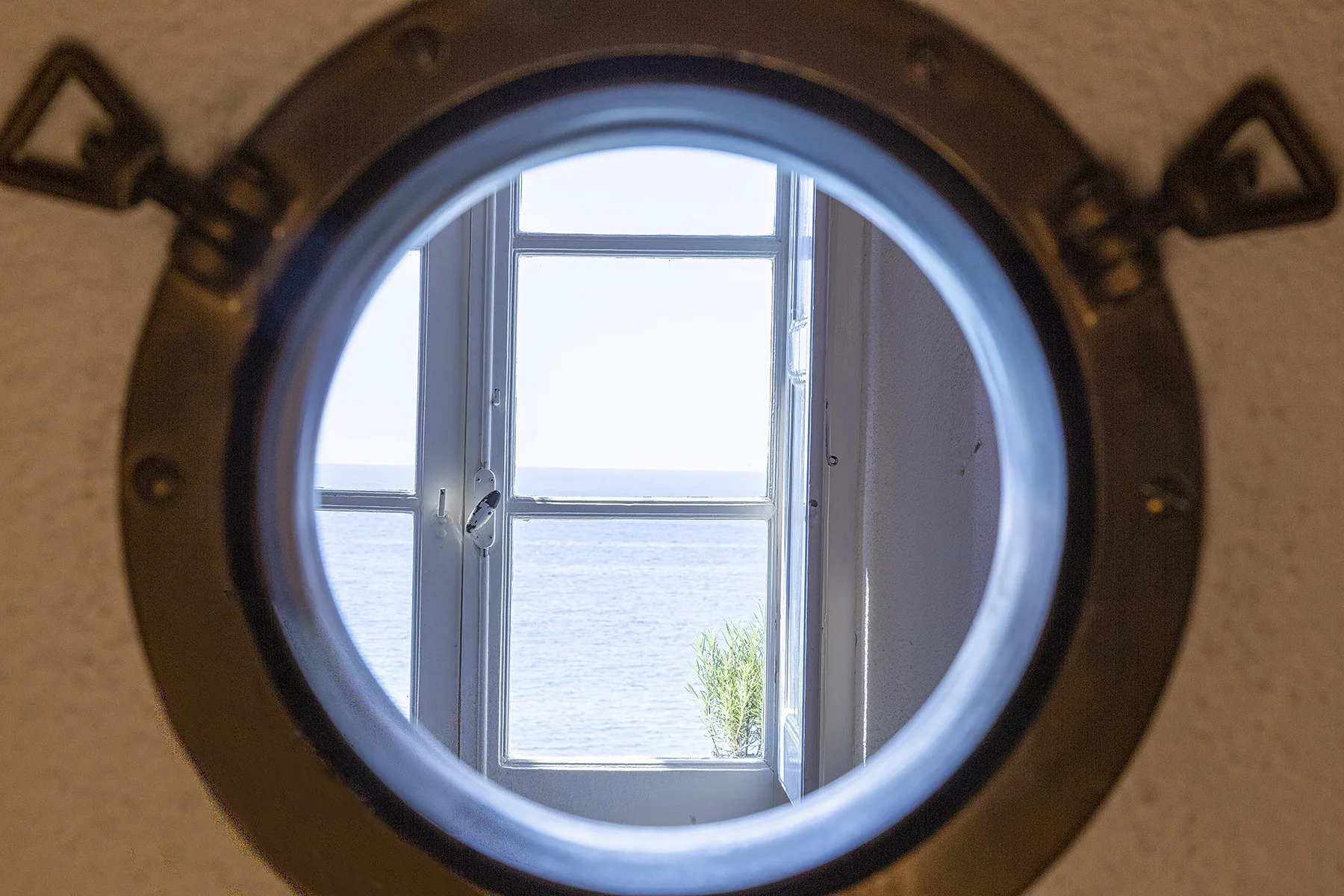 Un ojo de buey redondo enmarca una ventana abierta con vista al agua.