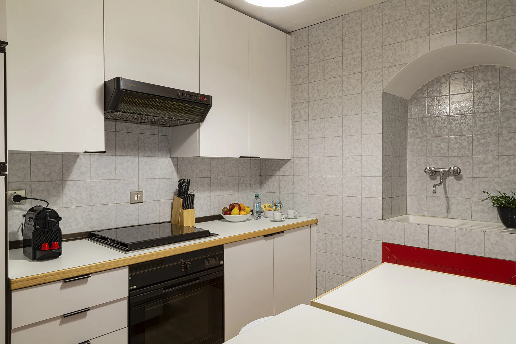Una cocina compacta con gabinetes blancos, una placa negra y una zona de ducha con azulejos.