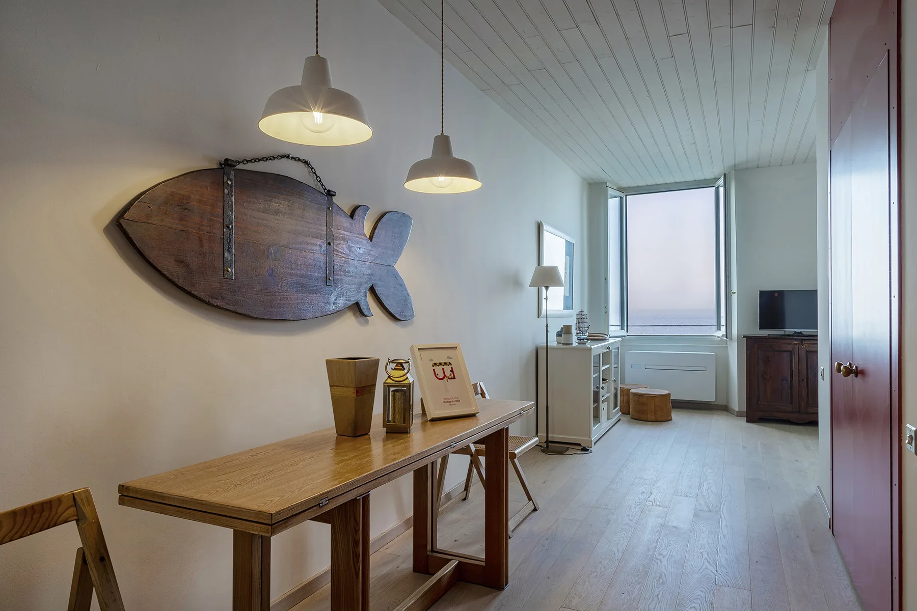 Una habitación luminosa con una mesa larga de madera y un pez decorativo en la pared.