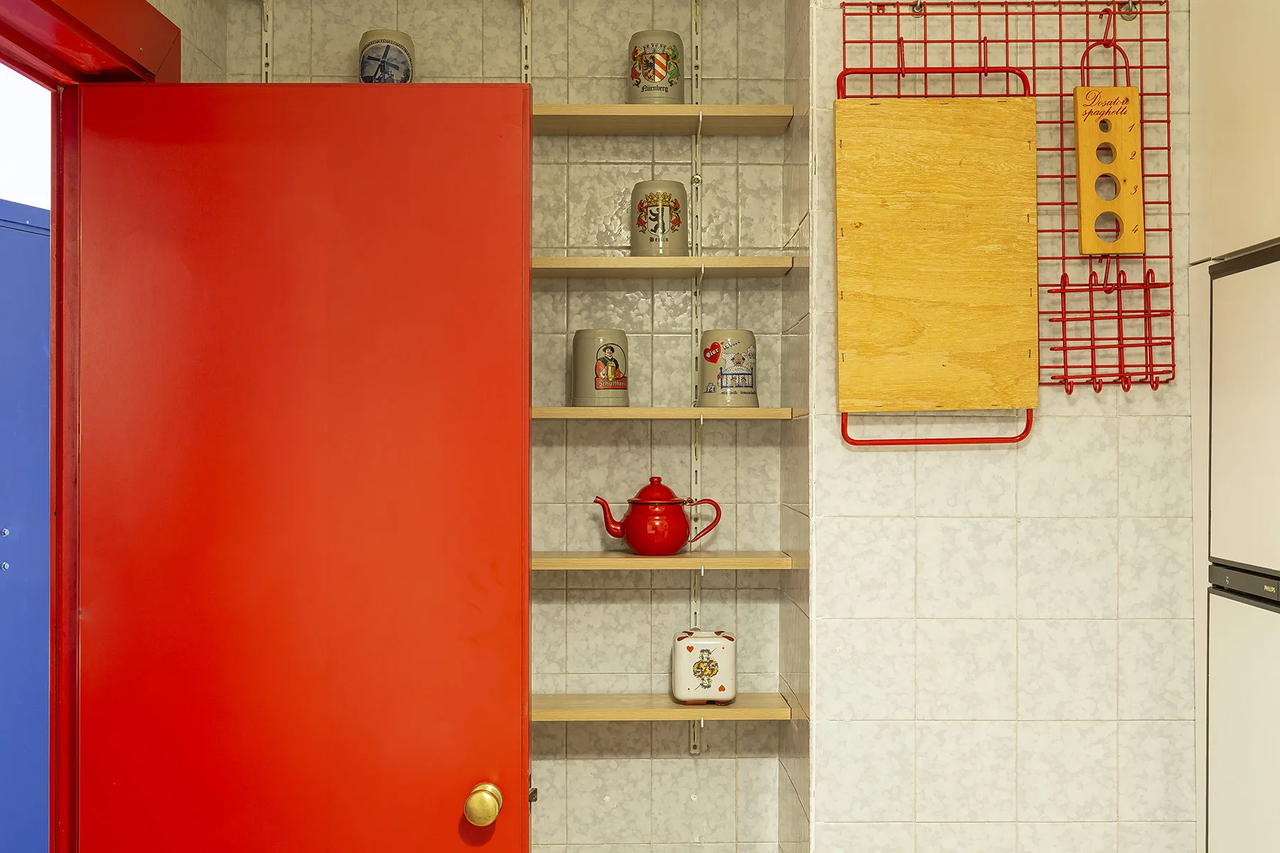 Una pared alicatada de cocina con estantes abiertos, frascos y una tetera roja.