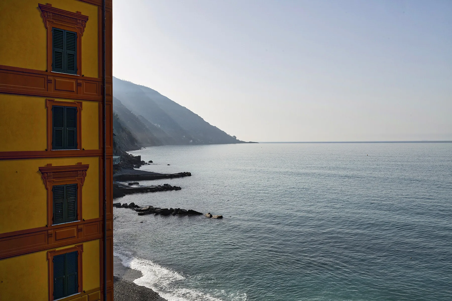 Una costa tranquila con una ladera montañosa junto al mar y un edificio amarillo en un extremo.