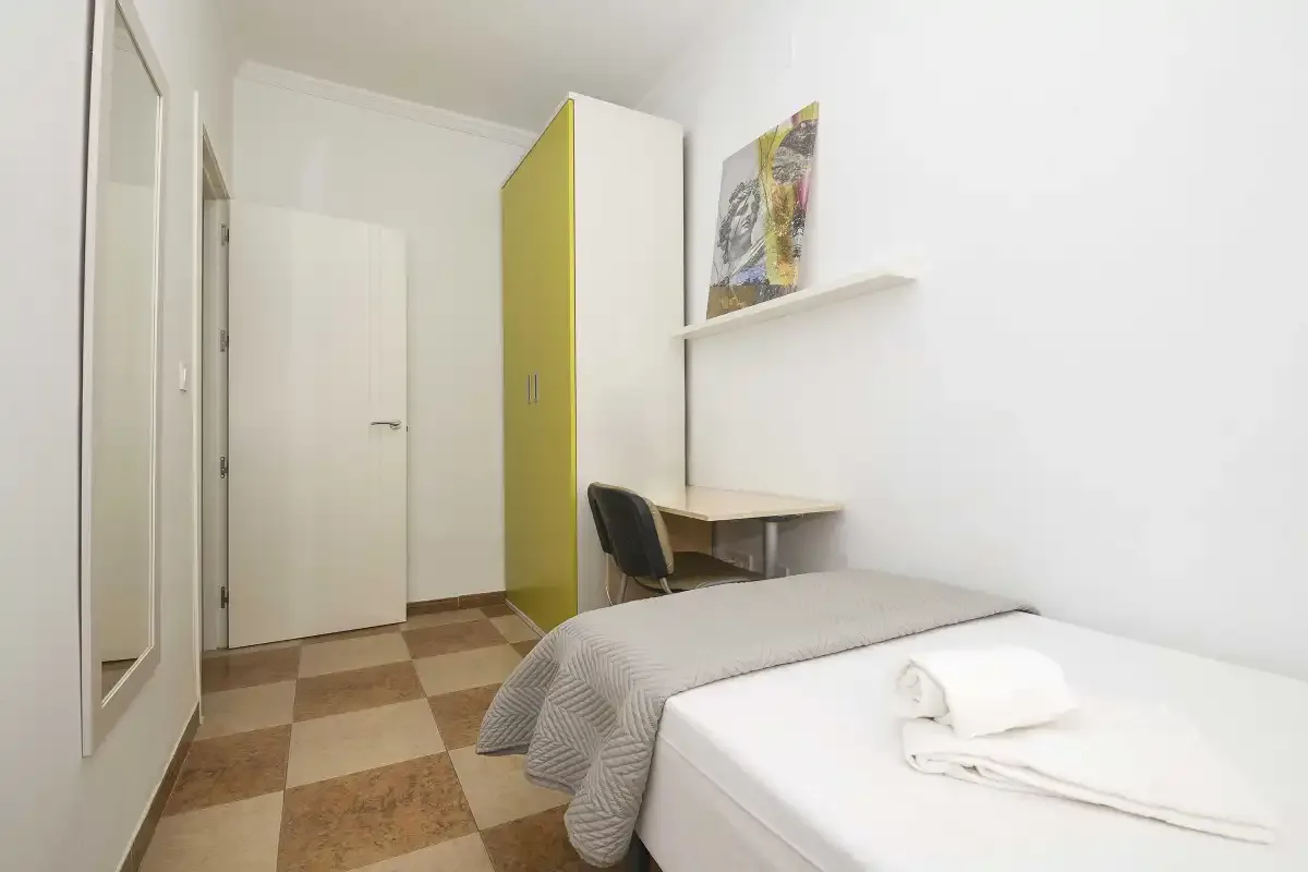 A bedroom with a bed, desk, and chair beside a wardrobe.