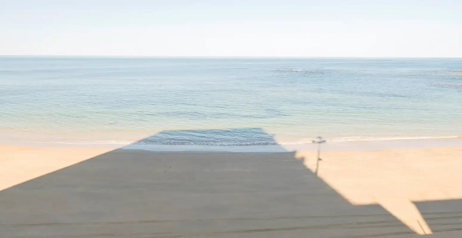 A wooden boardwalk leads across the beach toward calm water.
