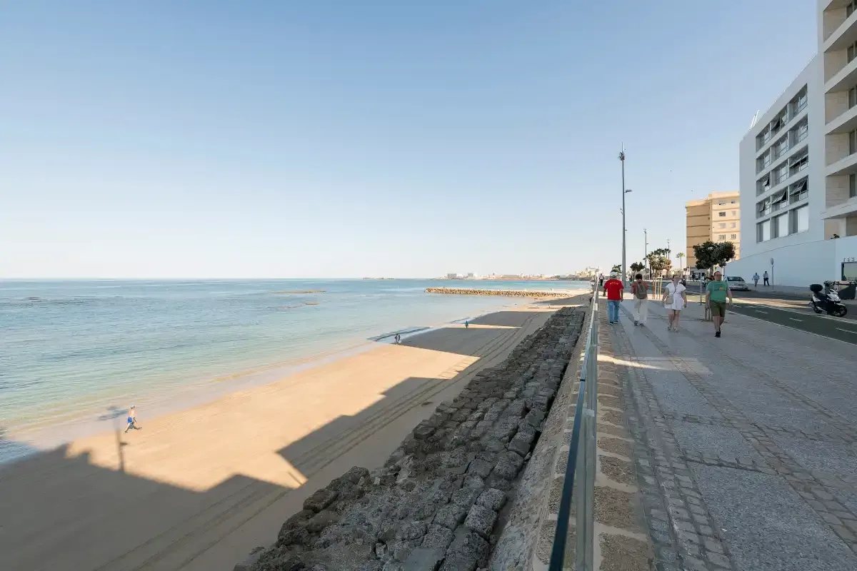 A seaside promenade runs beside a sandy beach and calm water.