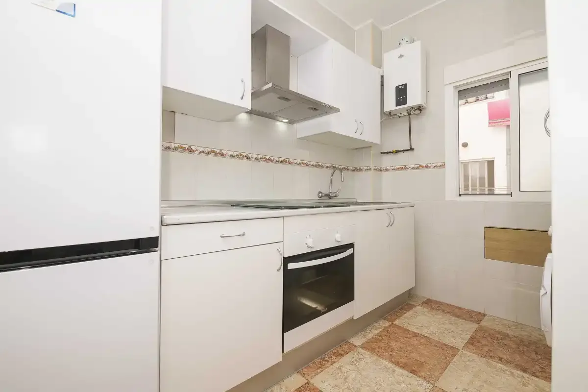 A bright kitchen with white cabinets, a stove, and a window.