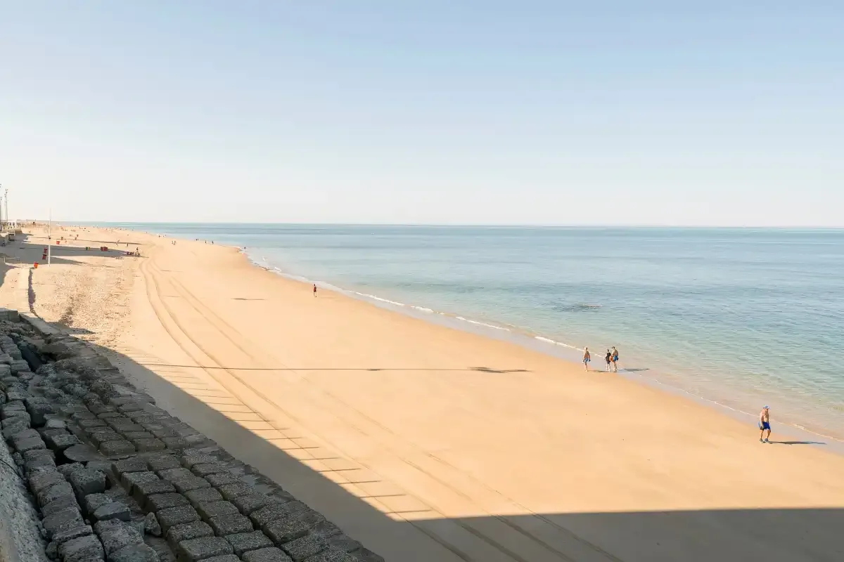 A broad sandy beach borders calm blue water beneath a clear sky.