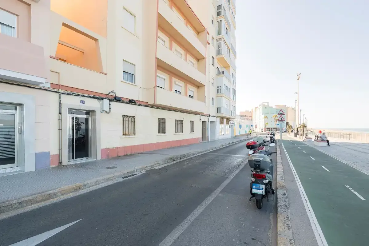 A city street runs beside apartment buildings, with scooters parked along the curb.