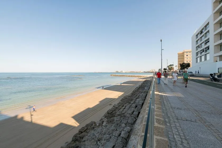 A seaside promenade runs alongside a sandy beach and calm water.