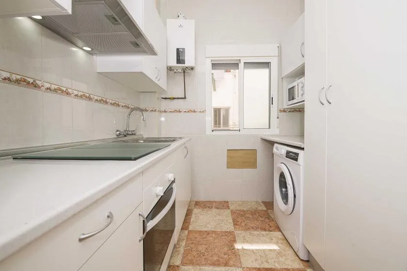 A bright kitchen with a cooktop, sink, and washing machine.