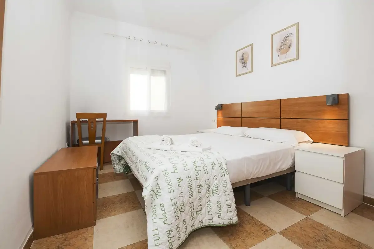 A bedroom with a double bed, bedside tables, and a desk by the window.