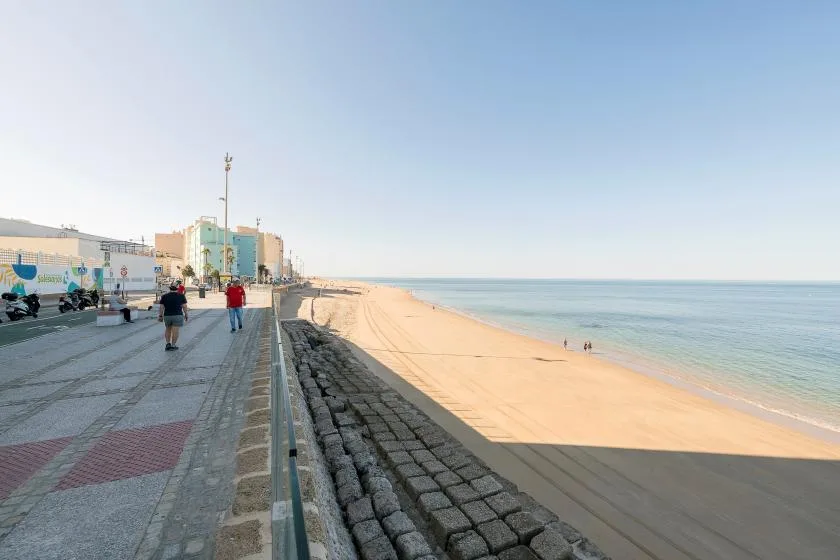 A seaside promenade runs beside a sandy beach and calm water.