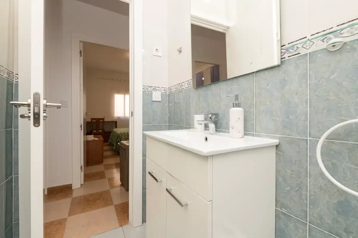 A bathroom with a sink and mirror beside an open doorway.