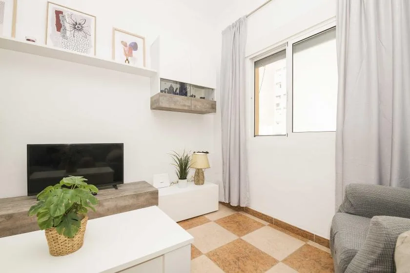 A bright living room with a television, low table, and large curtained window.