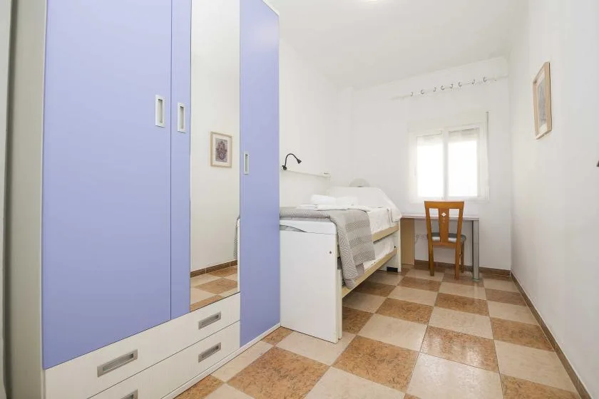 A bright bedroom with a bed, a wardrobe, and a desk by the window.