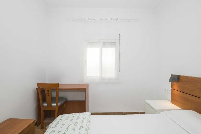 A bedroom with a bed, a desk, and a window.