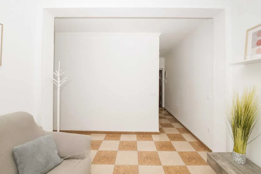 A bright living area opens onto a narrow hallway, with checkered floor tiles.