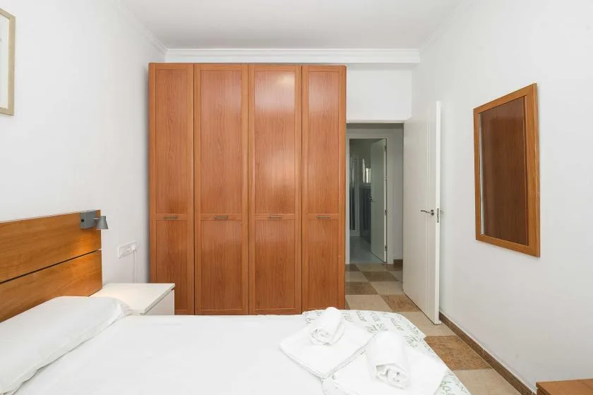 A bedroom with a large wooden wardrobe and a bed with white linens.