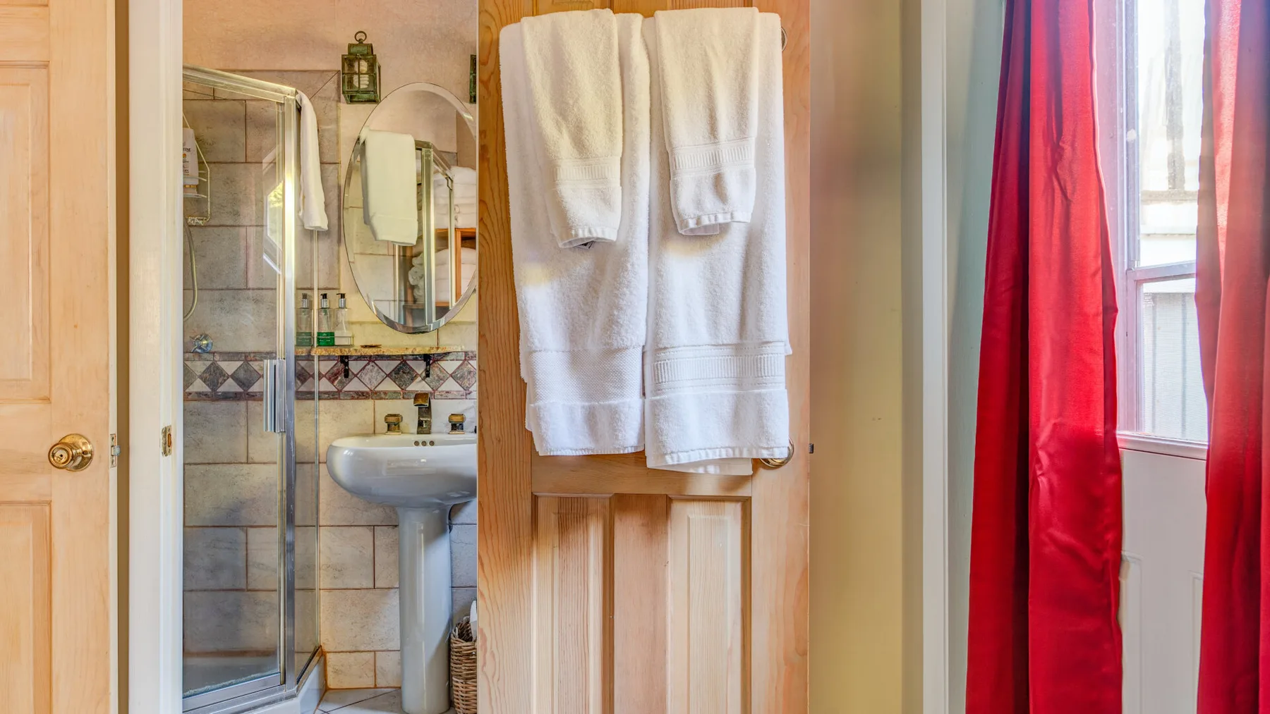 Un baño con lavabo, ducha y toallas colgadas en la puerta.