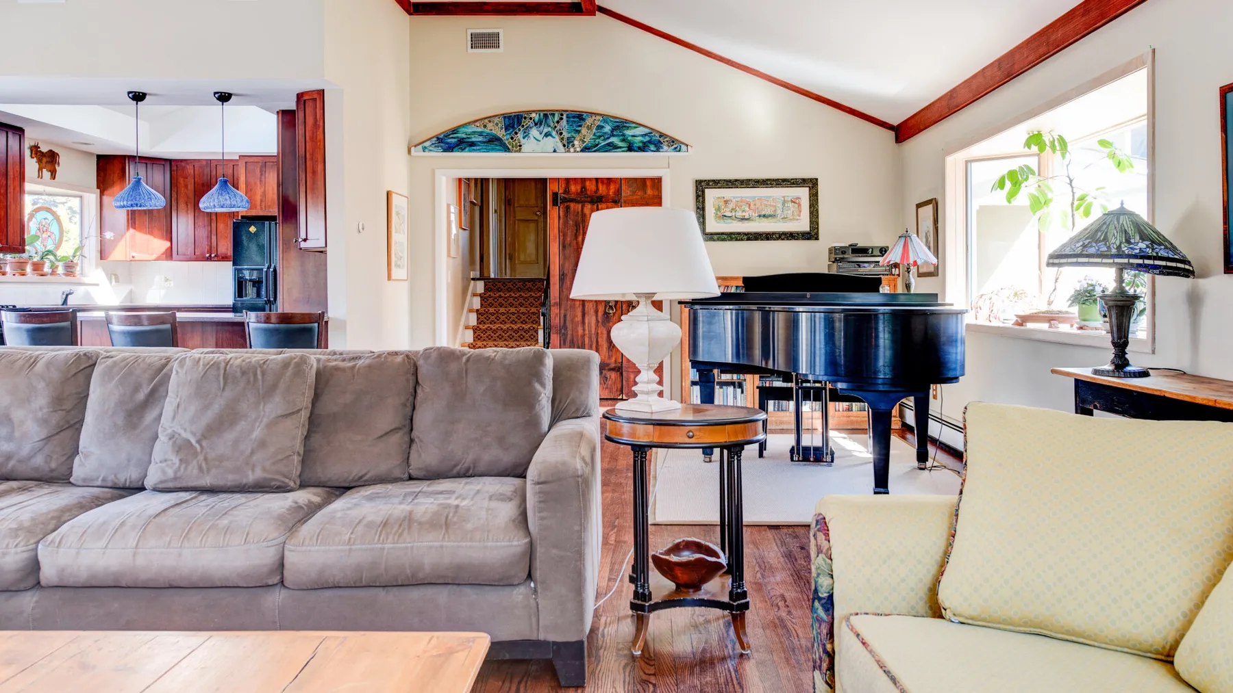 A bright living room with a sofa, piano, and large windows.