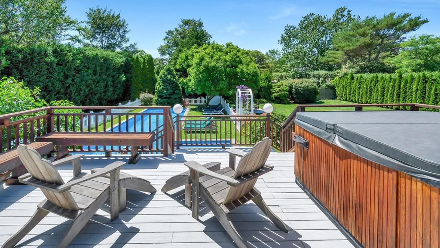 Una terraza de madera con asientos reclinables da a una piscina y un jacuzzi.